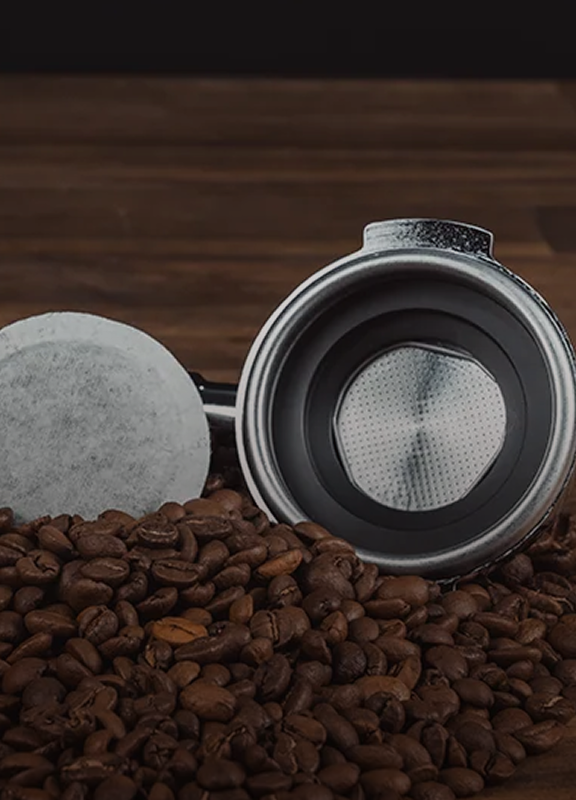 Coffee pod and portafilter basket lying on coffee beans