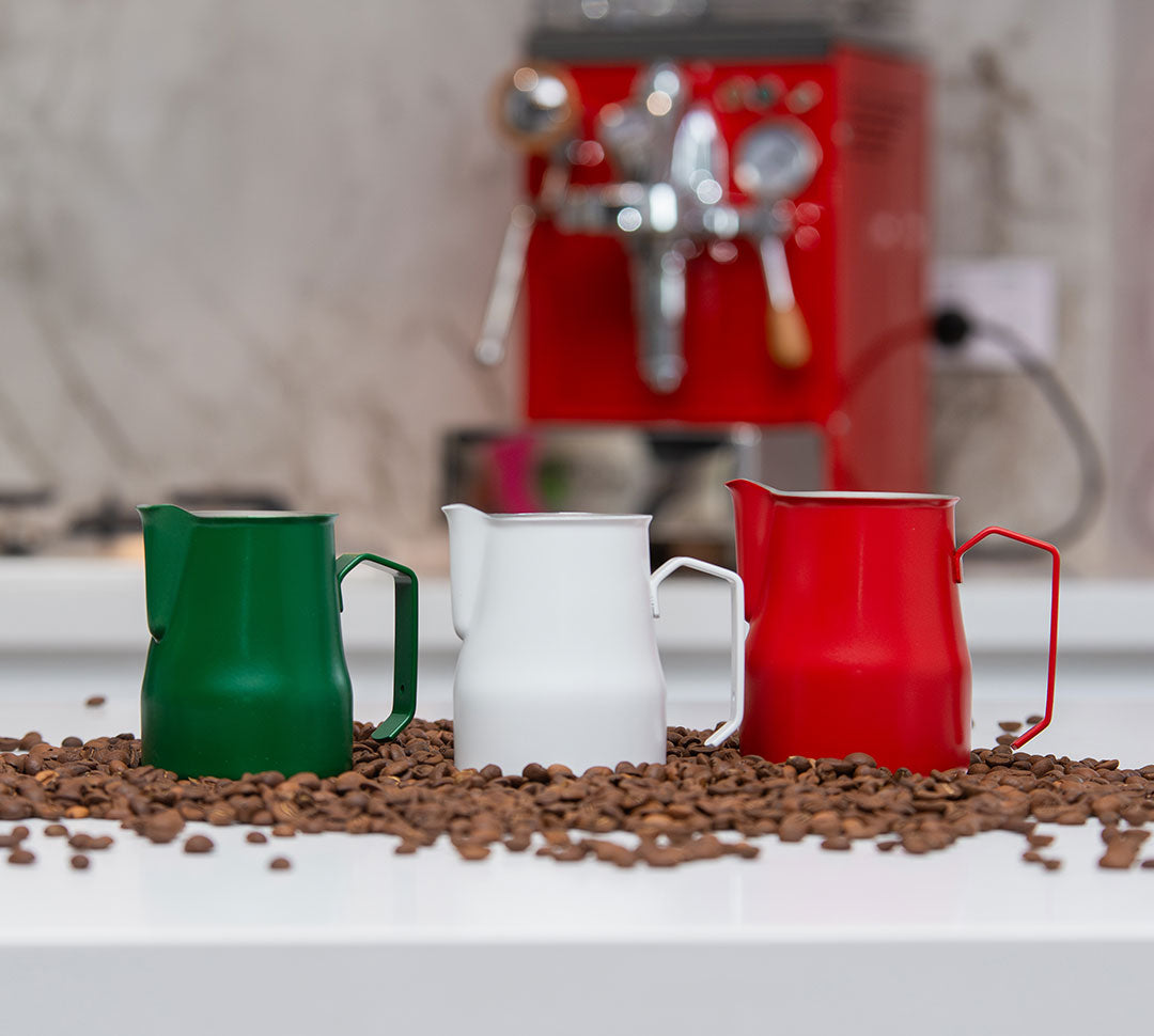 Colored milk jugs in green, white, and red, each with curved handle and spout