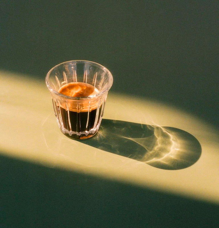Clear glass filled with a Bottega paper pod espresso coffee on a green surface with a soft shadow