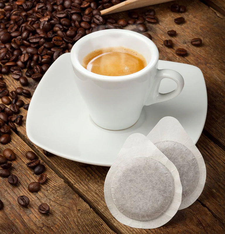 White cup of espresso with coffee beans and coffee paper pods on a wooden surface